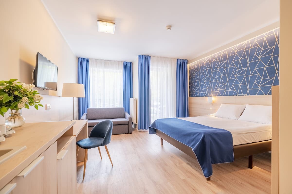 Ein modernes Hotelzimmer mit einem Bett, einem Schreibtisch mit Stuhl, einer Couch und einem Fernseher.