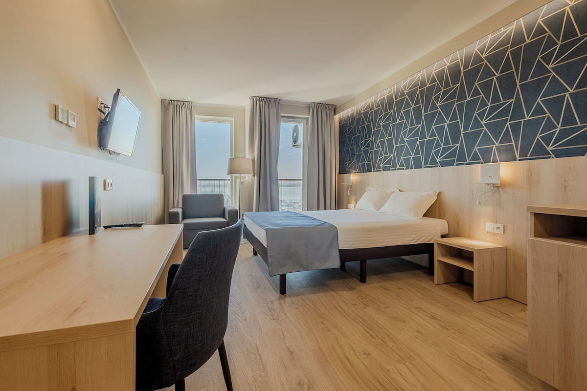 Ein modernes Hotelzimmer mit Bett, Schreibtisch, Stuhl und einer Wand mit geometrischem Muster.
