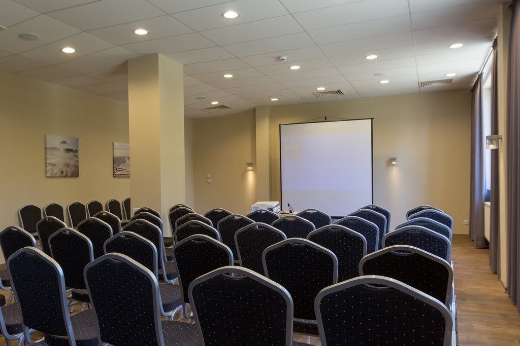 A conference room with rows of chairs, a projector screen, and a whiteboard.