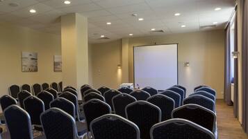 A conference room with rows of chairs, a projector screen, and a whiteboard.