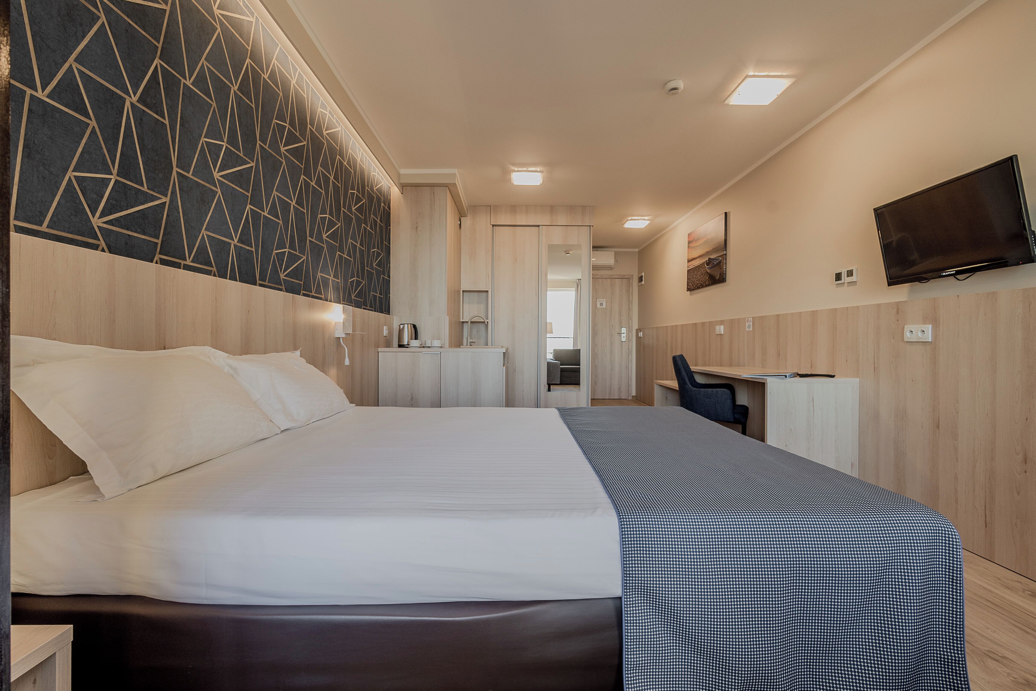 A hotel room with a large bed, a desk, a TV, and a modern wall design.
