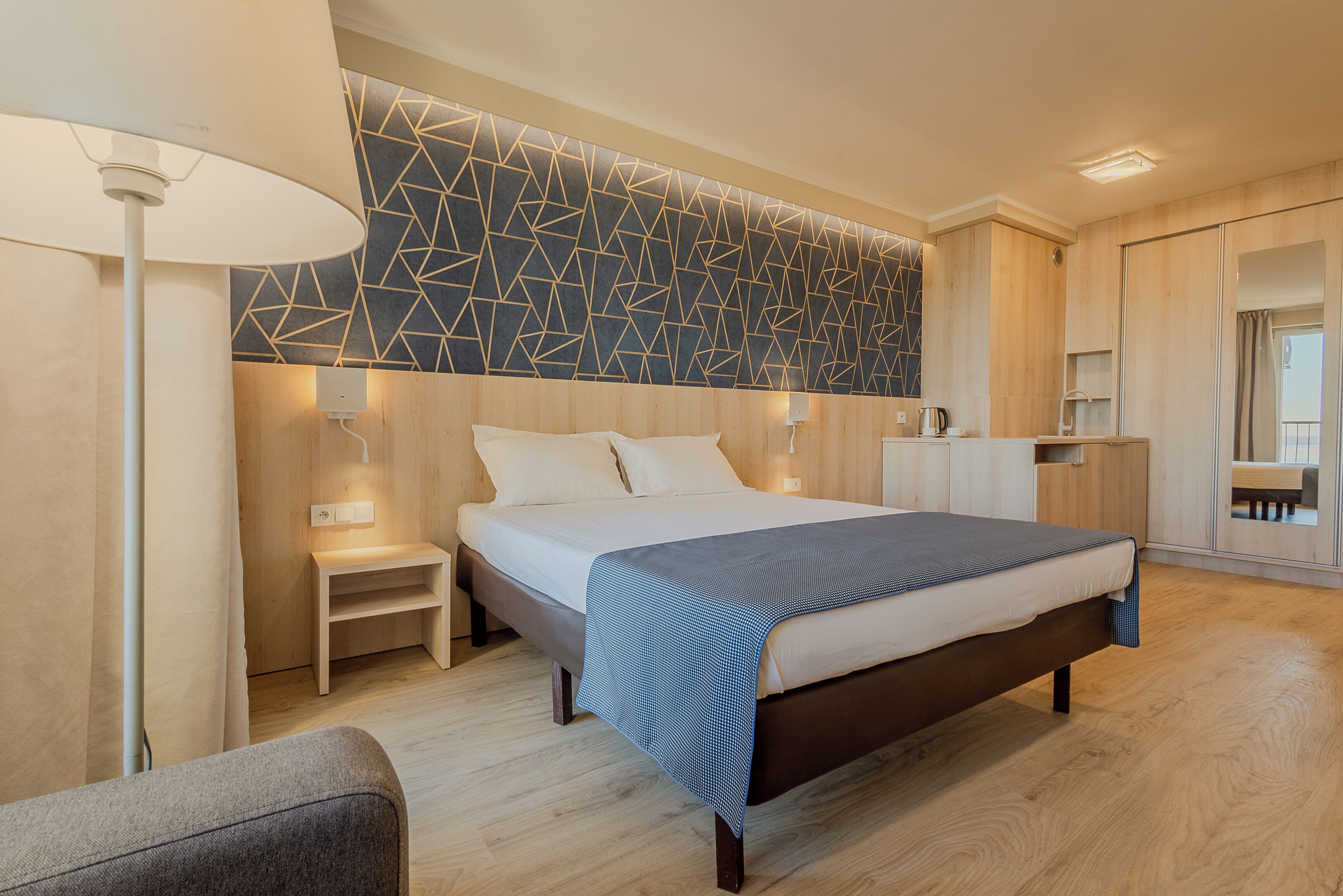 Un dormitorio moderno con una cama, mesitas de noche, una lámpara y una pared con estampado geométrico.
