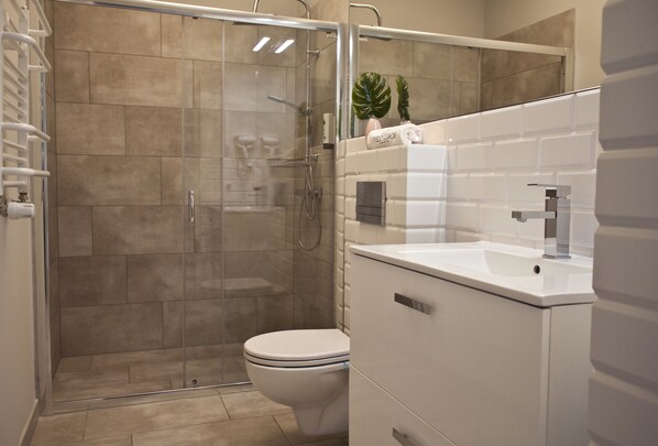 A modern bathroom with a glass-enclosed shower, a white toilet, and a white sink with a mirror above it. - Aparthotel Miedzyzdroje (Miedzyzdroje)