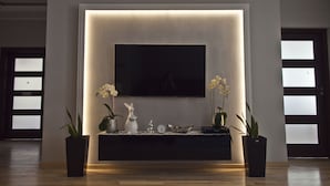 A modern living room with a flat-screen TV mounted on a wall, surrounded by decorative items and plants. - Aparthotel Miedzyzdroje (Miedzyzdroje)