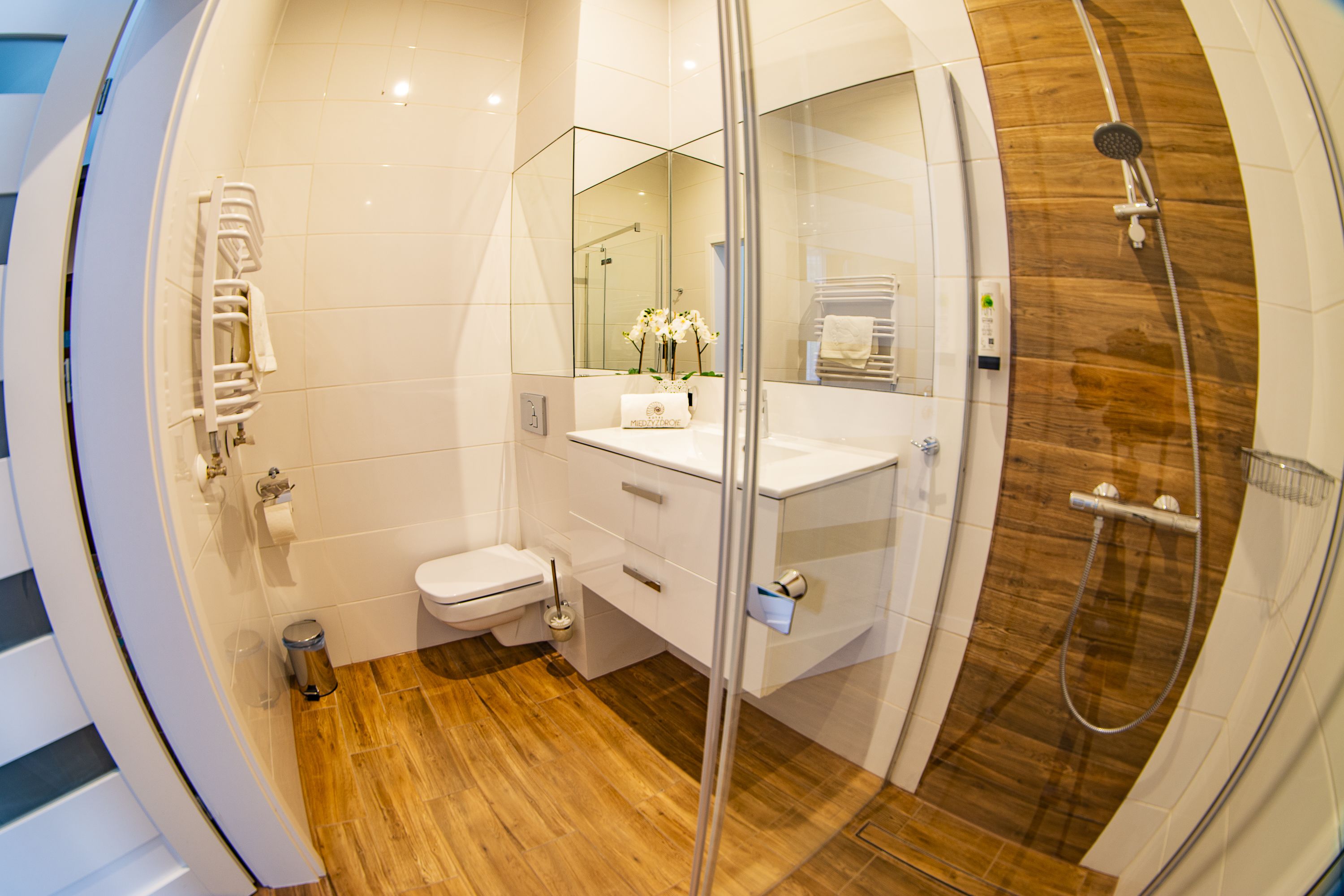 Une salle de bain moderne avec une douche à parois de verre, un plancher en bois, un lavabo blanc et des toilettes.