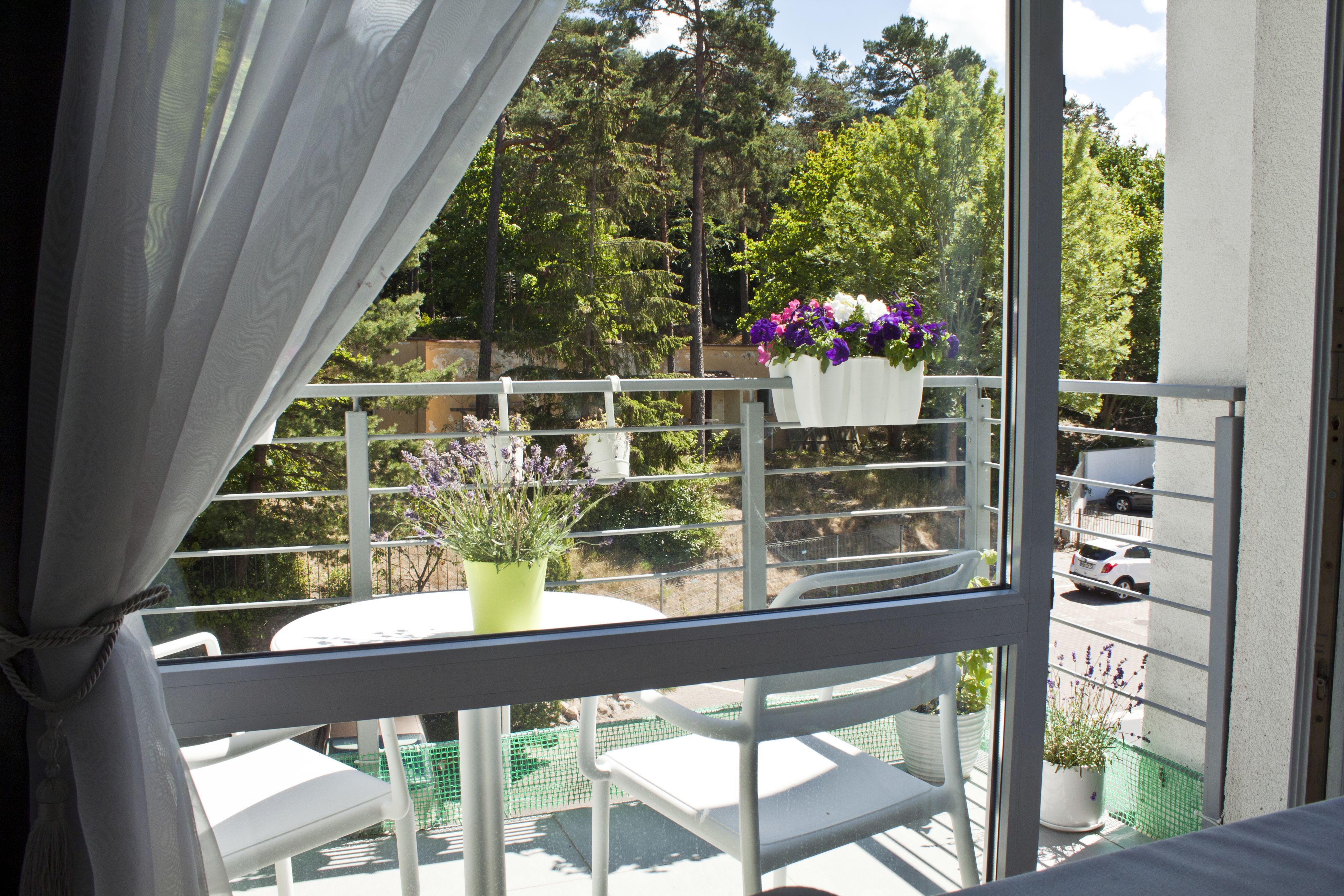 A balcony with white chairs, a small table, and potted plants.