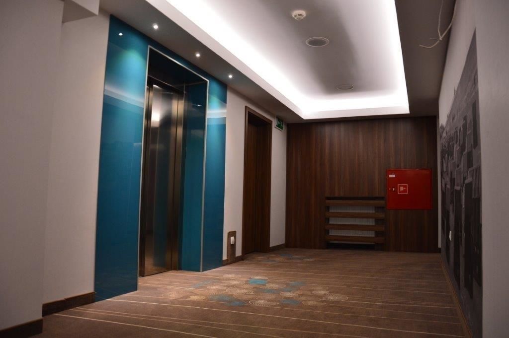 Un pasillo moderno con suelo de madera, un ascensor azul y un extintor rojo.