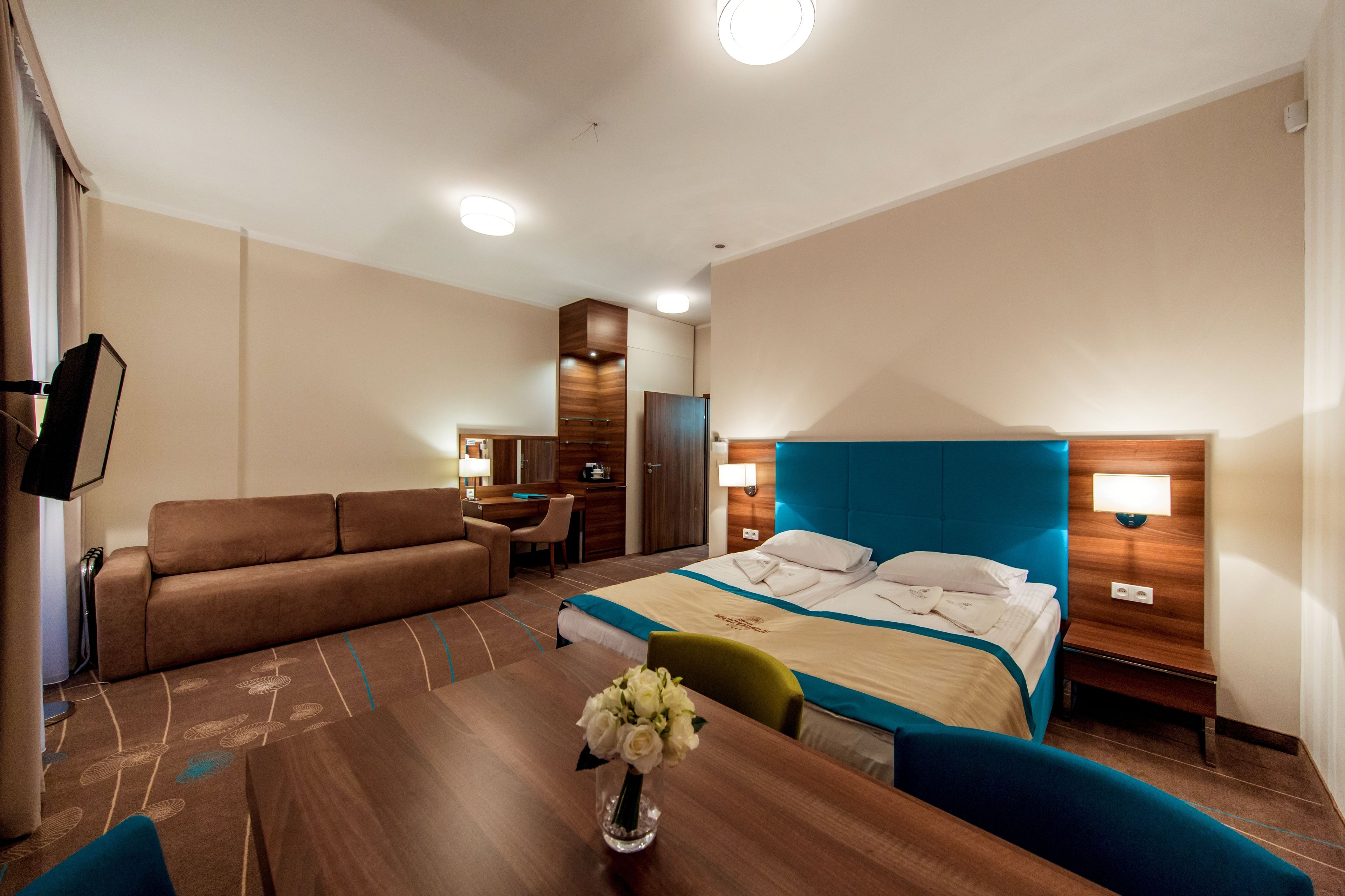 A hotel room with a bed, a sofa, a desk, and a dining table.
