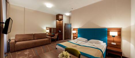 A hotel room with a bed, a sofa, a desk, and a dining table.