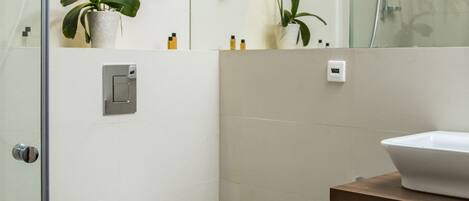 A modern bathroom with a glass-enclosed shower, a white toilet, a wooden vanity with a sink, and two potted orchids on the wall.