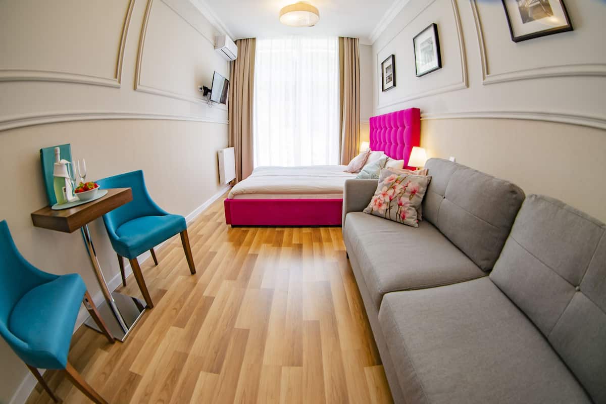 A modern hotel room with a bed, a grey sofa, a small table with chairs, and a TV on the wall.
