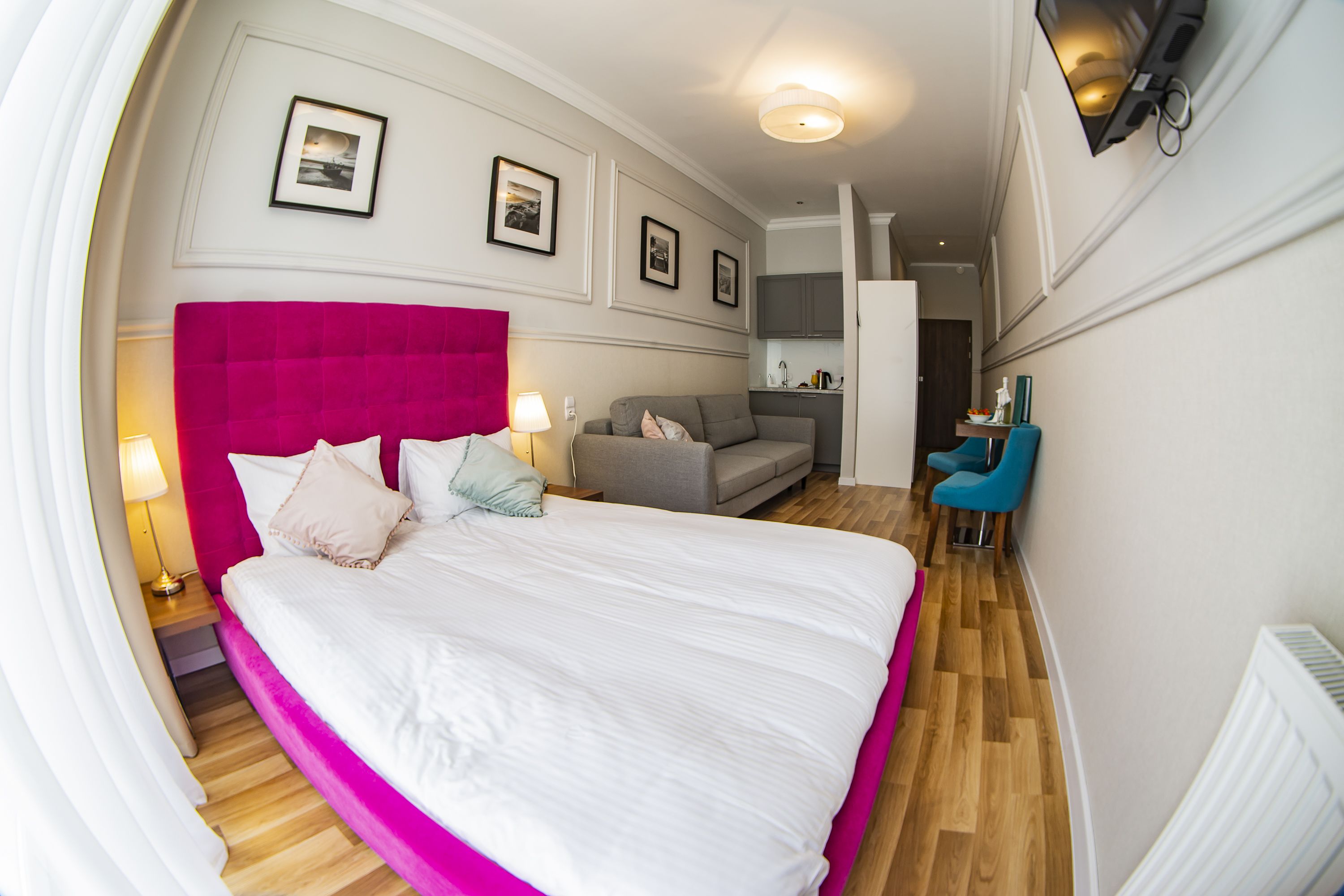 A bedroom with a large bed, a sofa, a desk with a chair, and a kitchenette.