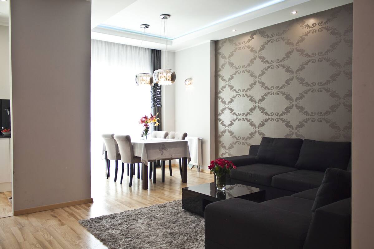 A modern living room with a dark sofa, a coffee table, and a dining area with a table and chairs.