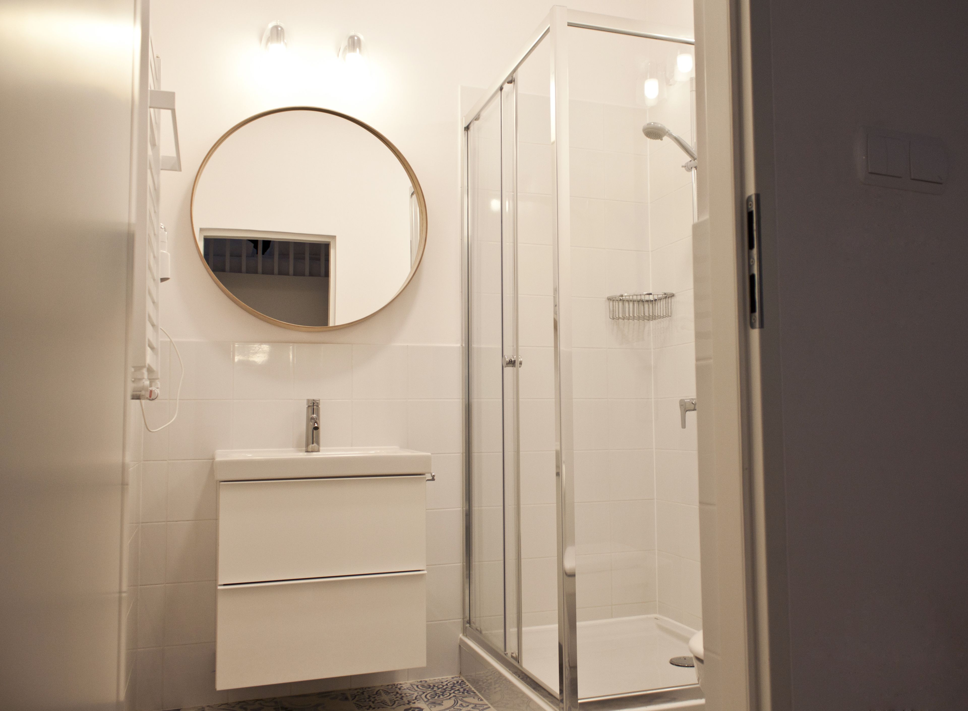 Un baño moderno con un espejo redondo, un lavabo blanco y una ducha con mampara de vidrio.