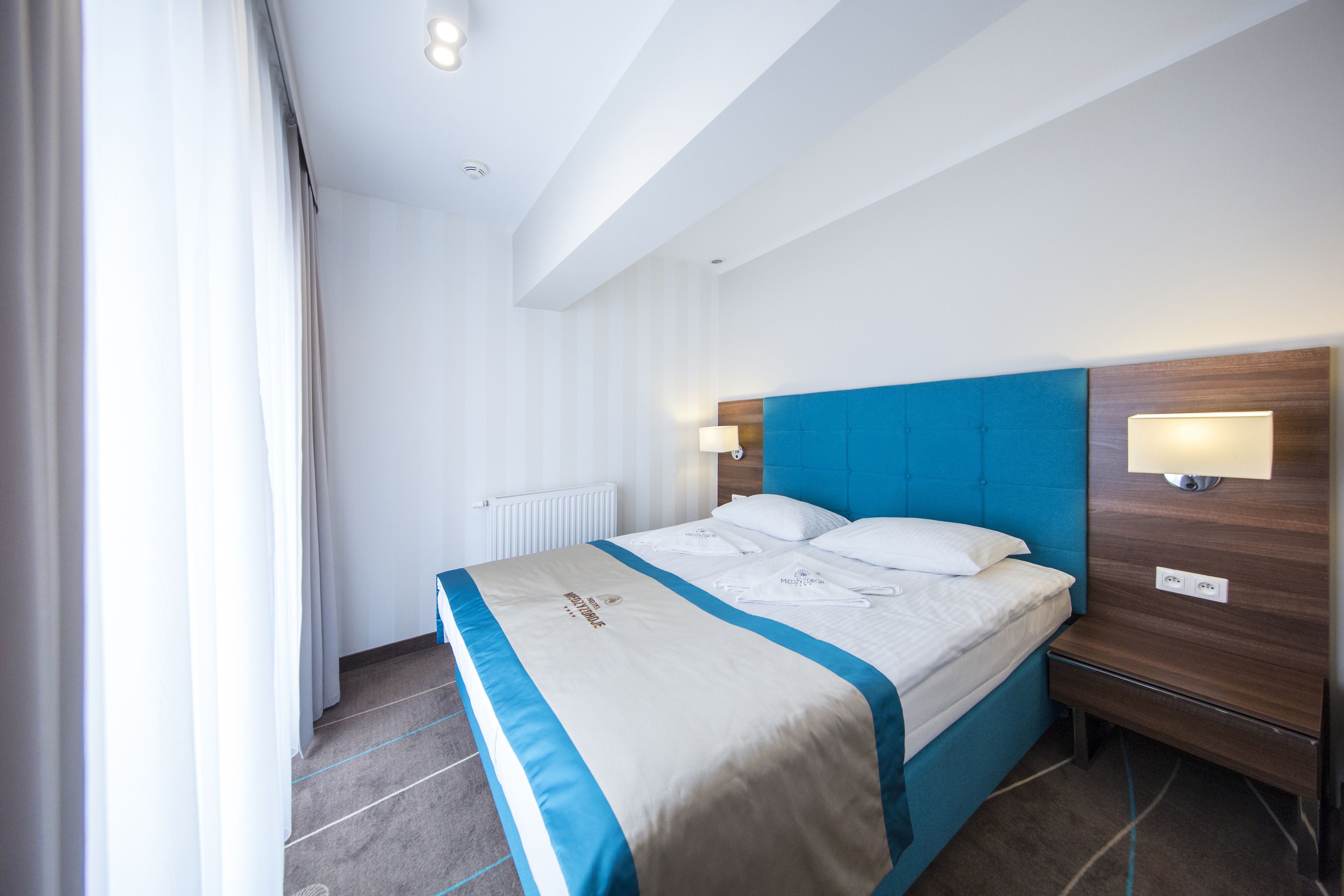 Una habitación de hotel moderna con una cama grande, cabecera de madera y una mesita de noche con lámpara.