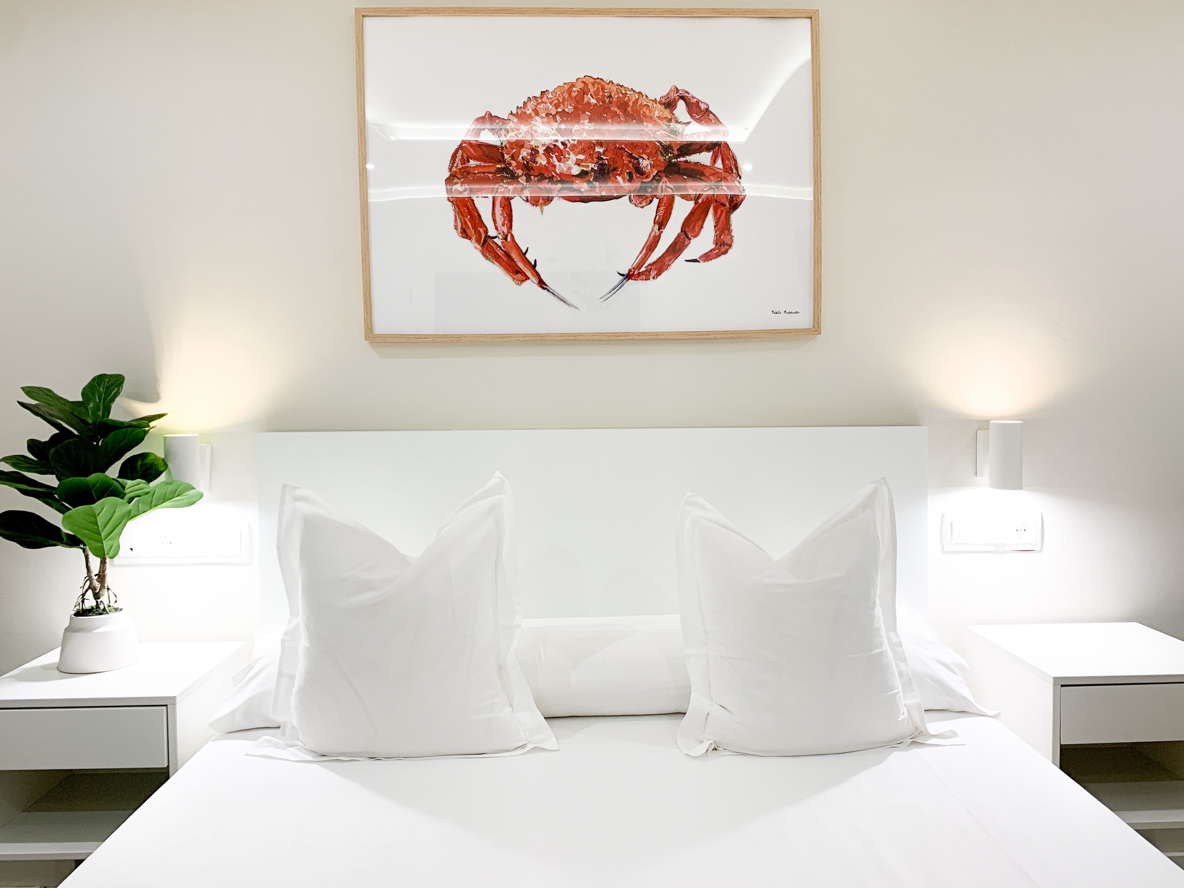 A neatly made bed with white bedding and pillows, a framed artwork of a crab on the wall, and a potted plant on the nightstand.
