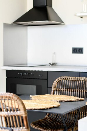 A modern kitchen with a black range hood, white cabinets, and a dining area with wicker chairs and woven placemats. - Hotel Celta (Vigo)