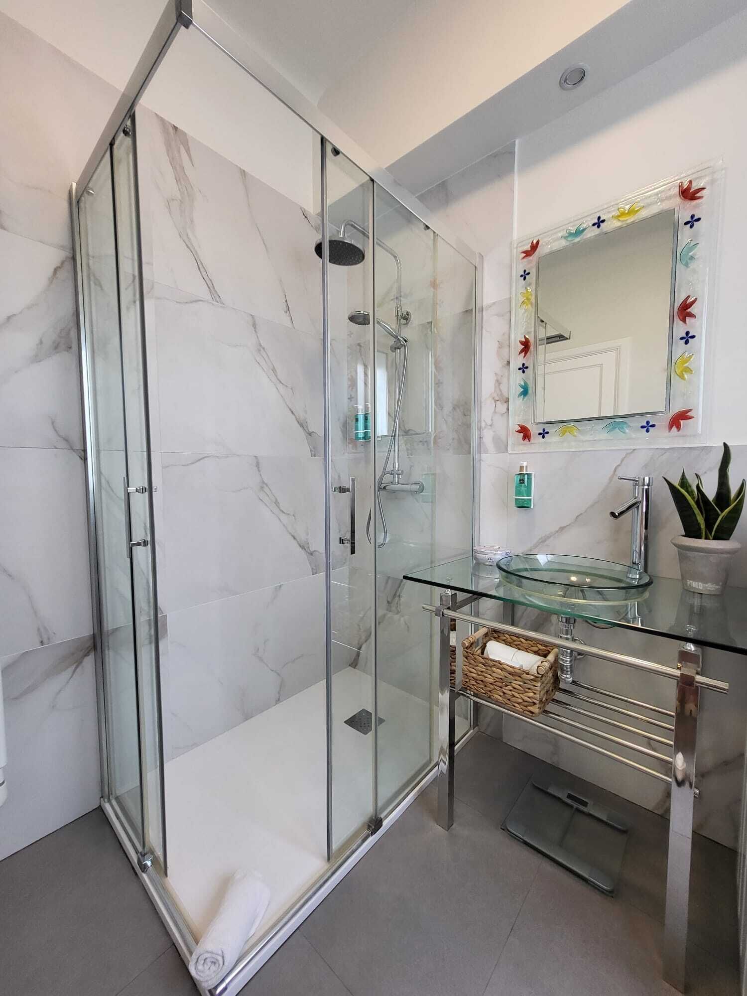 A modern bathroom with a glass-enclosed shower, a glass sink, and a decorative mirror.