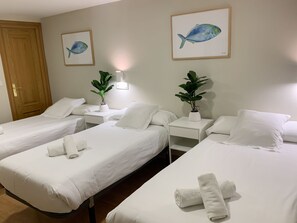 A hotel room with three single beds, each with white linens and towels. There are two potted plants on the nightstands, and two framed fish paintings on the wall. - Hotel Celta (Vigo)