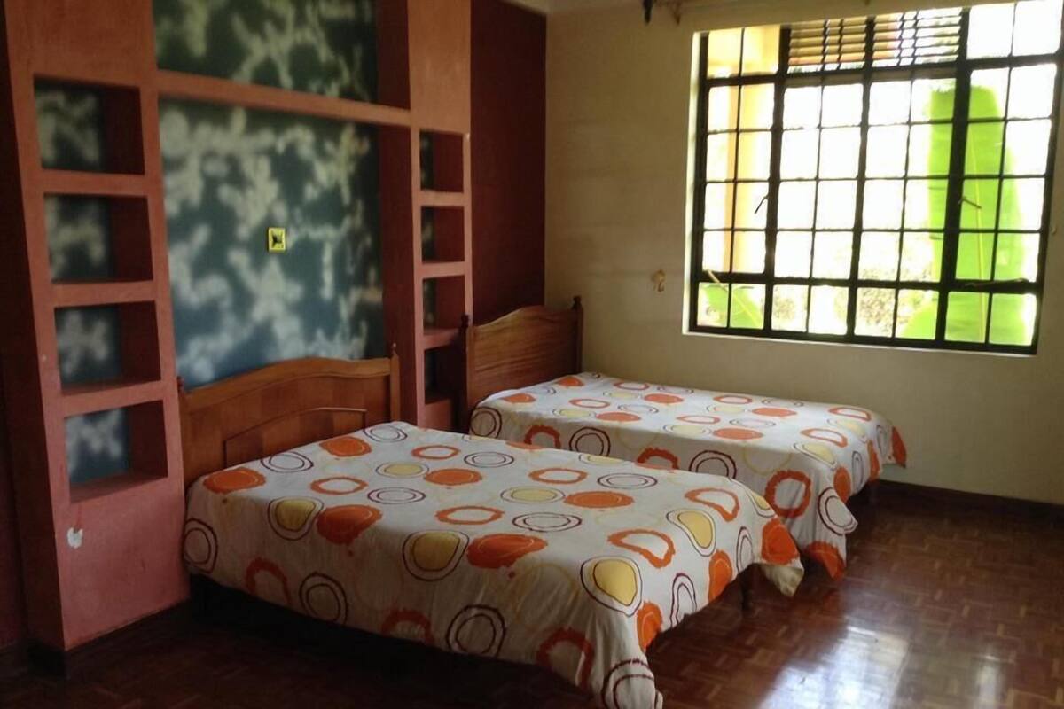 Una habitación con dos camas, una ventana con barrotes y un cabecero de madera con estantes.