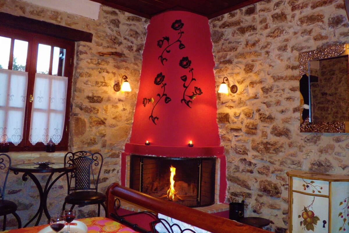 A stone-walled room with a fireplace, a mirror, and a table with chairs.