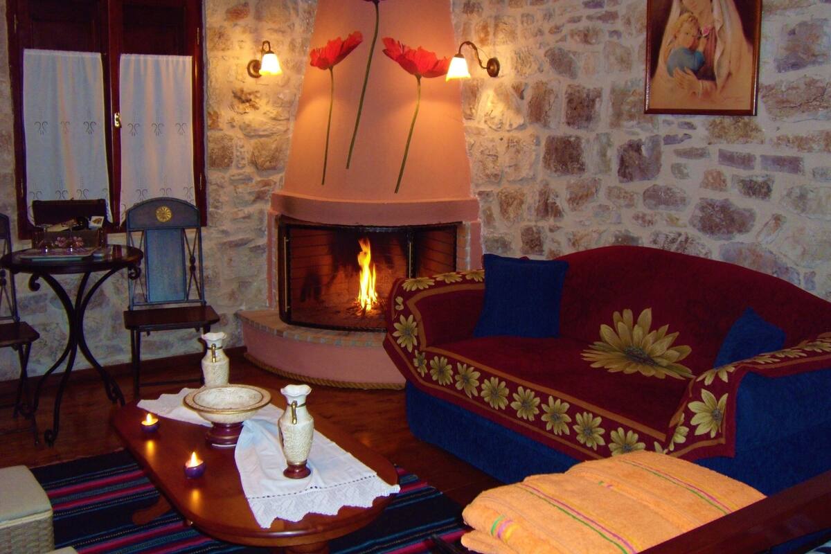 A cozy living room with a stone wall, a fireplace, a sofa, and a table with candles.