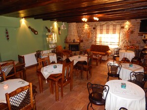 A cozy dining area with wooden furniture, stone walls, and a fireplace. - Arhontiko Kordopati Traditional Guesthouse (Tripoli)