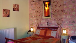 A bedroom with a bed, a nightstand, a chair, a radiator, and a shower area. - Arhontiko Kordopati Traditional Guesthouse (Tripoli)