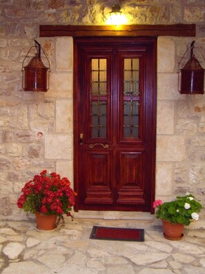 A wooden double door with glass panels, flanked by two lantern-style lights, set against a stone wall. - Arhontiko Kordopati Traditional Guesthouse (Tripoli)