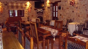 A rustic dining area with wooden furniture, stone walls, and a television mounted on the wall. - Arhontiko Kordopati Traditional Guesthouse (Tripoli)