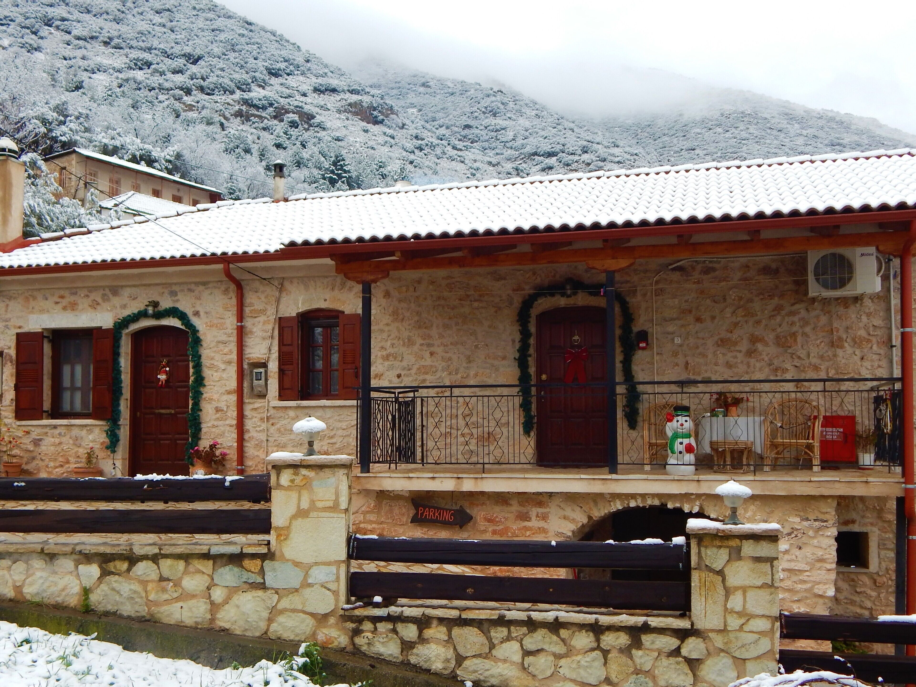 A stone building with a tiled roof, a wooden porch, and a sign indicating a parking area.