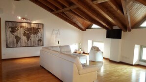 A spacious loft with a high ceiling, wooden beams, a large world map artwork, a white sofa, a small table with a plant, and a television mounted on the wall. - Donizetti Royal (Bergamo)
