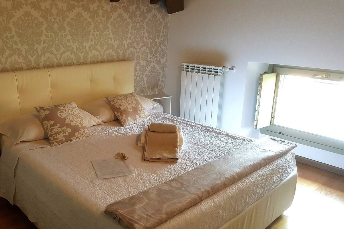 A neatly made bed with a patterned bedspread, several pillows, and a folded towel.