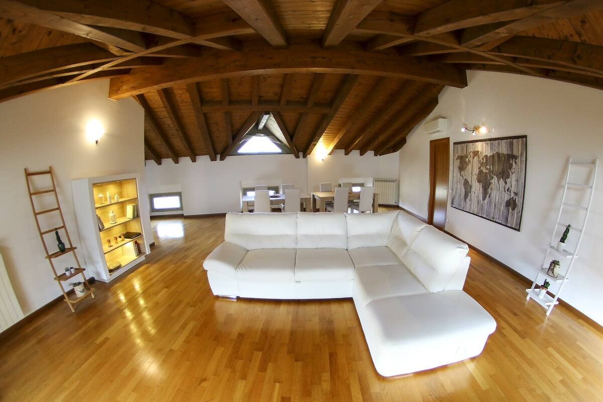 A spacious living area with a large white sectional sofa, wooden flooring, and a sloped ceiling with exposed beams.