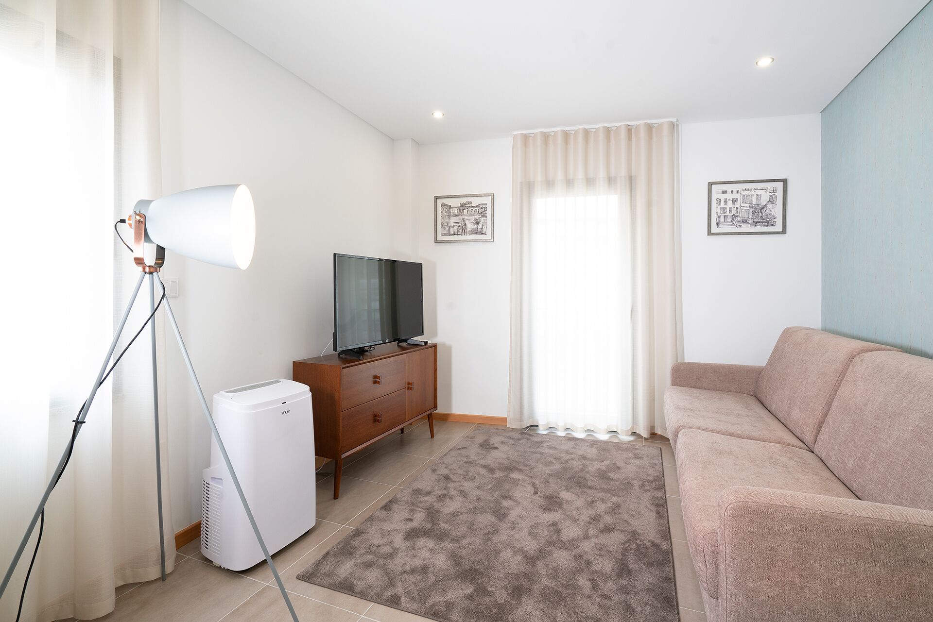 Un soggiorno con divano, televisore su mobile in legno, lampada e termosifone.