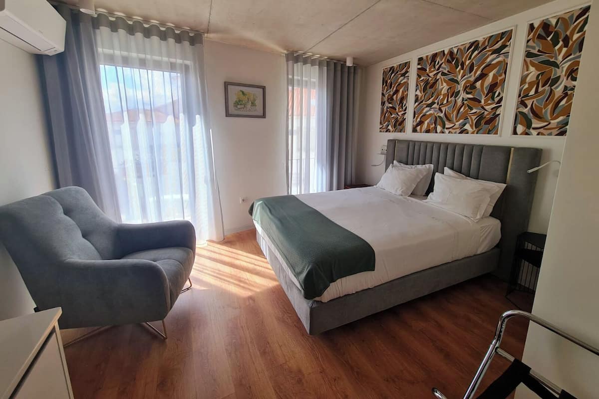 A hotel room with a bed, a chair, a picture on the wall, and a window with curtains.