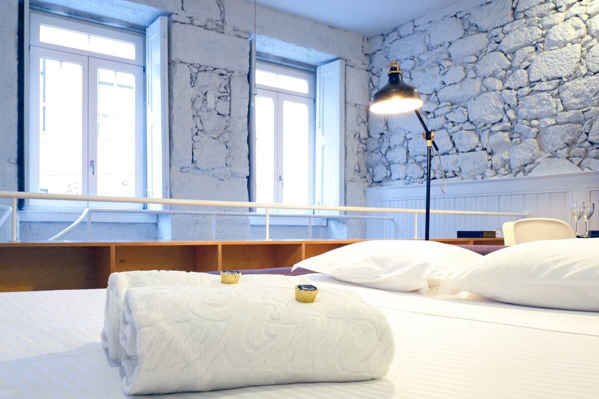 A hotel room with a large bed, a stone wall, and a window with a view.