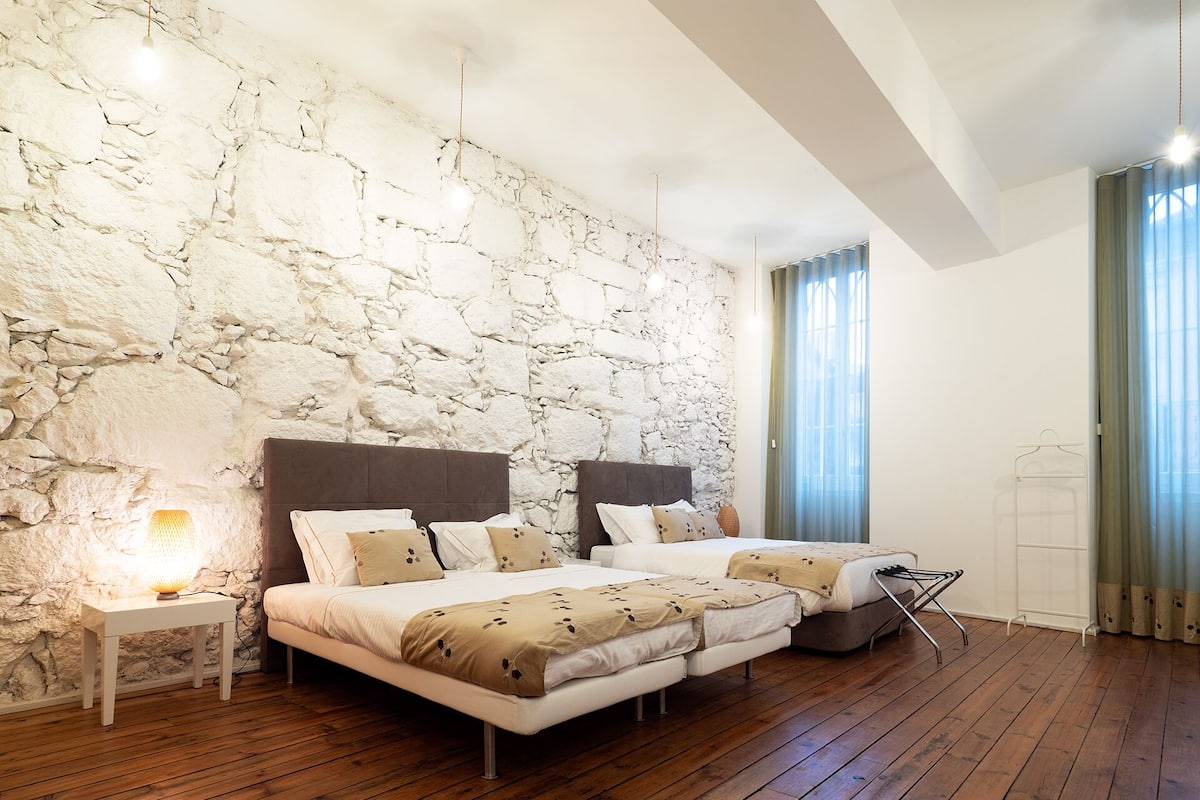 A bedroom with a stone wall, two beds, a bedside table with a lamp, and a hanging light fixture.