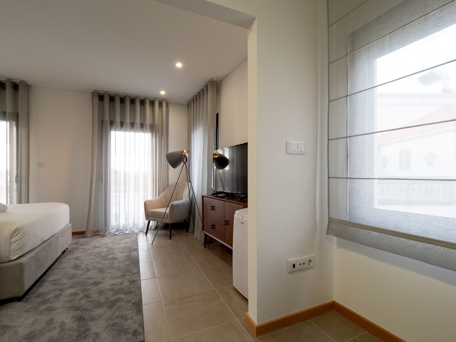 A hotel room with a bed, a desk with a chair, a TV, and a window with blinds.