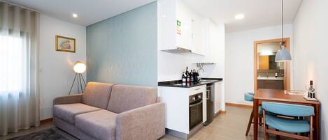 Un espacio habitable compacto con kitchenette, un sofá, una mesa de comedor con sillas y una pequeña zona de cocina.