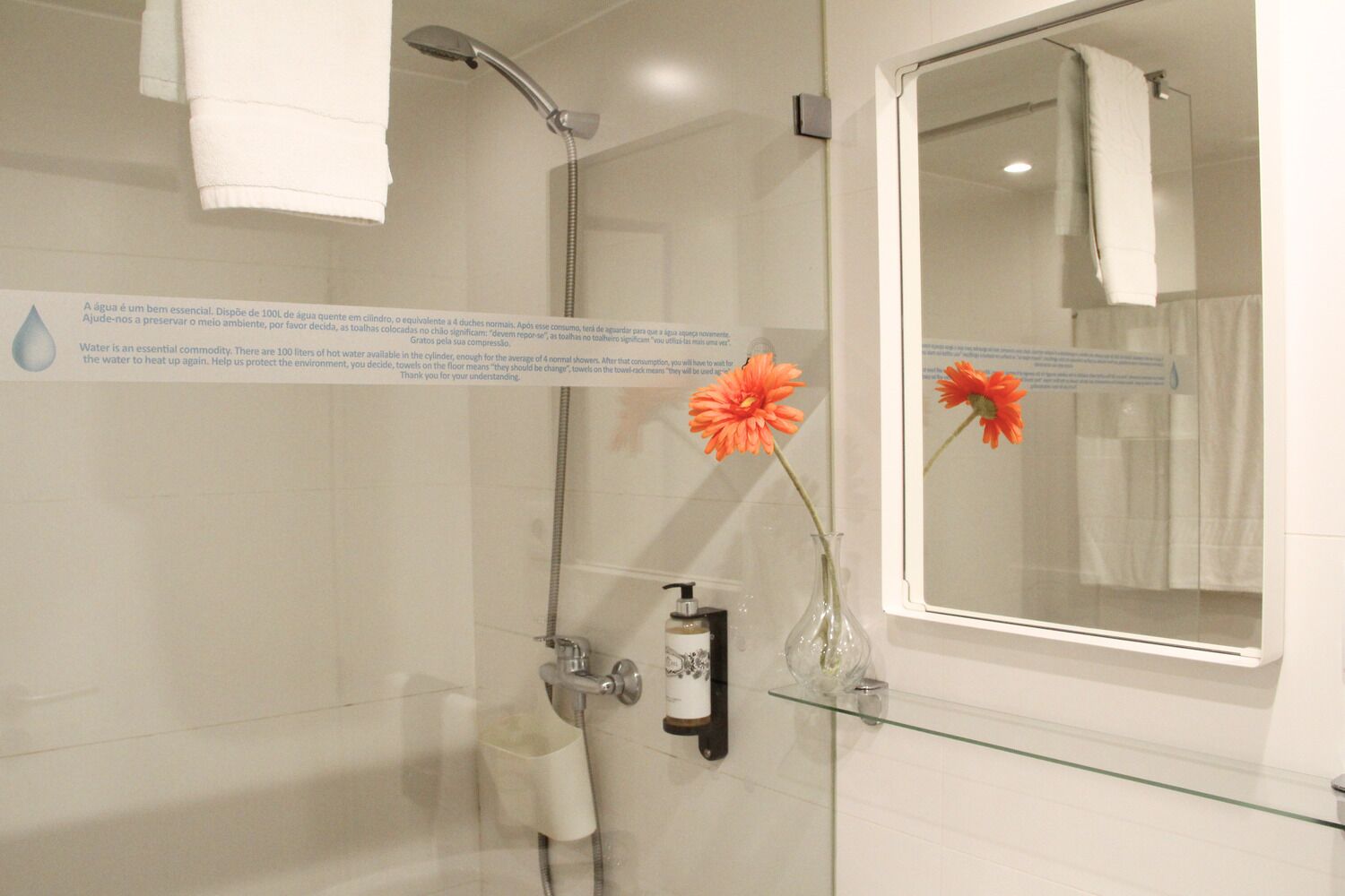 A modern bathroom with a glass shower enclosure, a large mirror, and a vase with a flower.