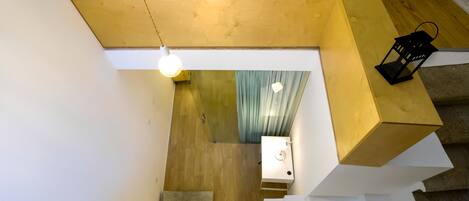 A modern staircase with a wooden finish, a light fixture, and a view of a room with a curtain.