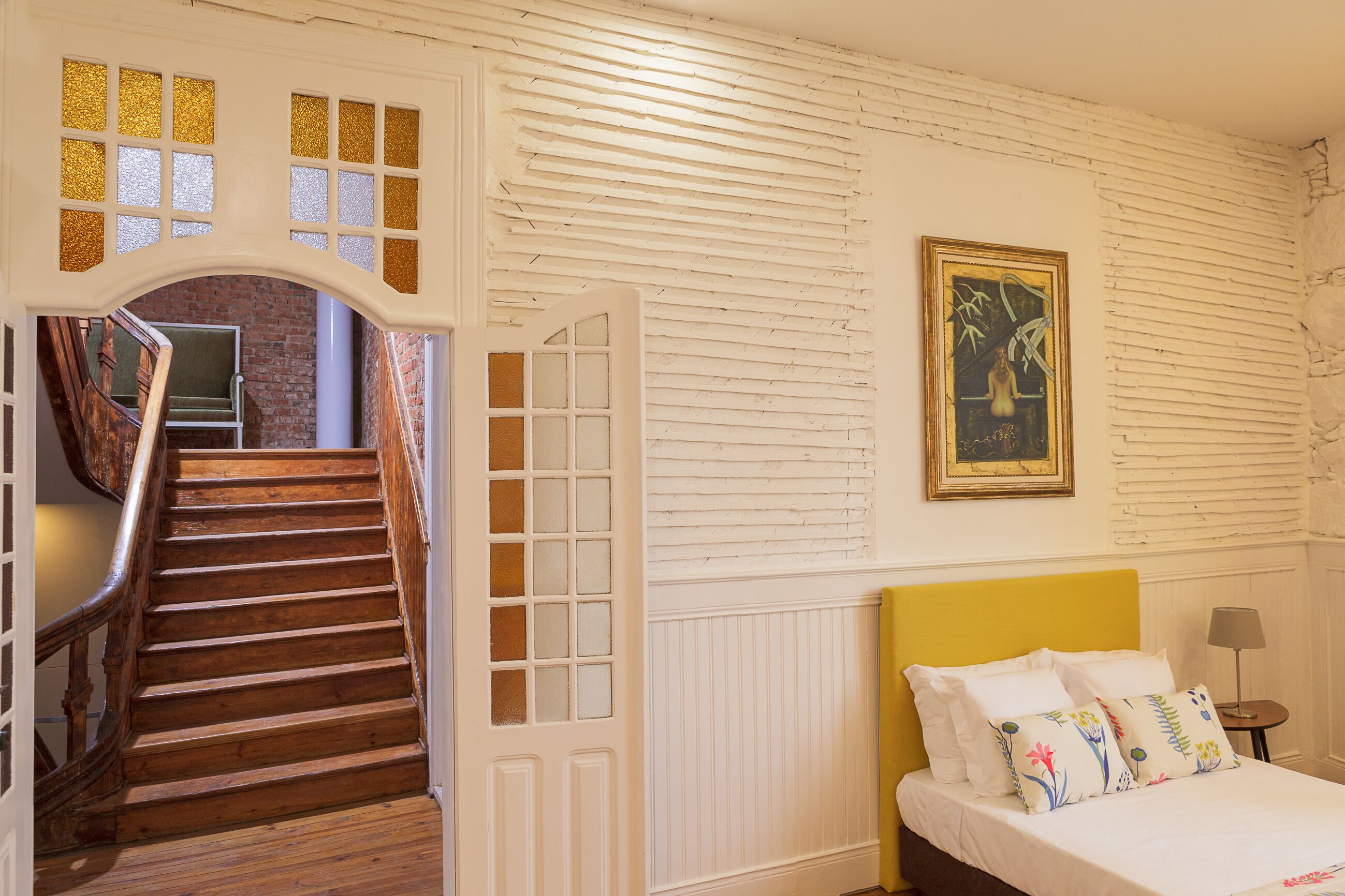 A bedroom with a wooden staircase, a bed with white bedding, and a framed painting on the wall.