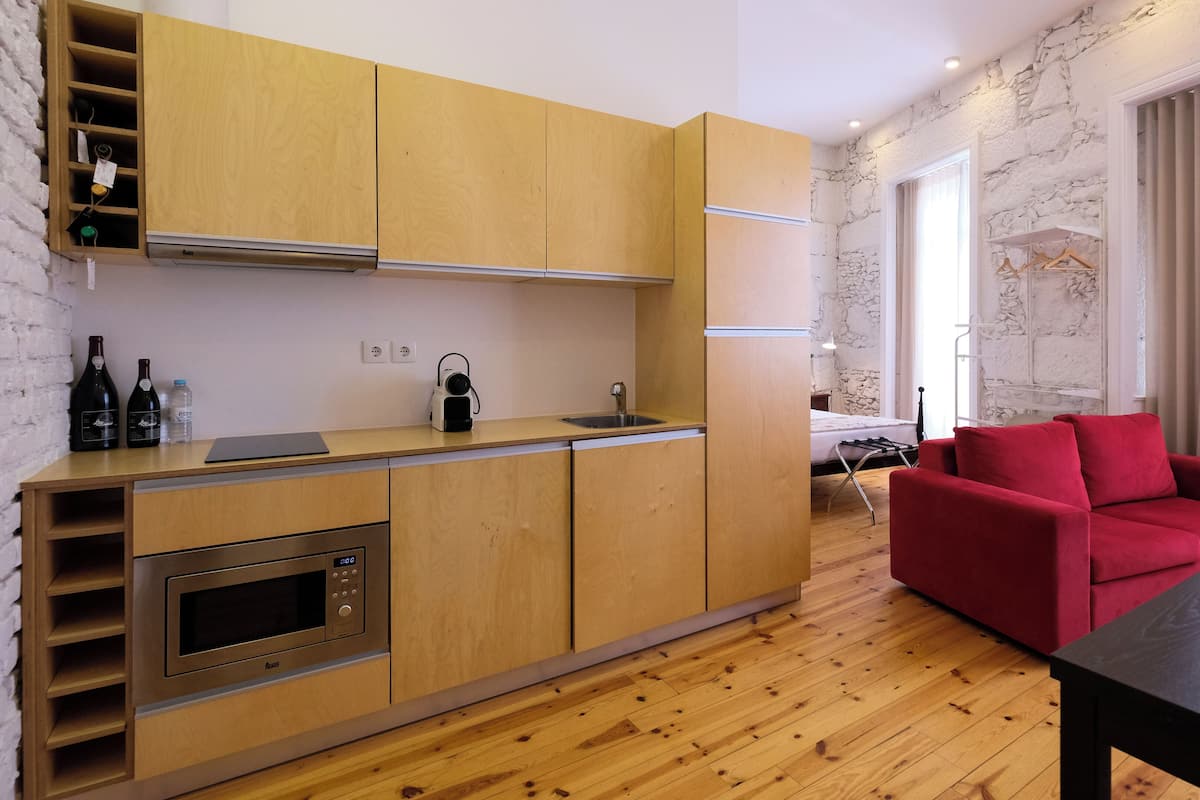 A modern kitchen with wooden cabinets, a built-in oven, and a sink. There is a red sofa and a table in the living area.