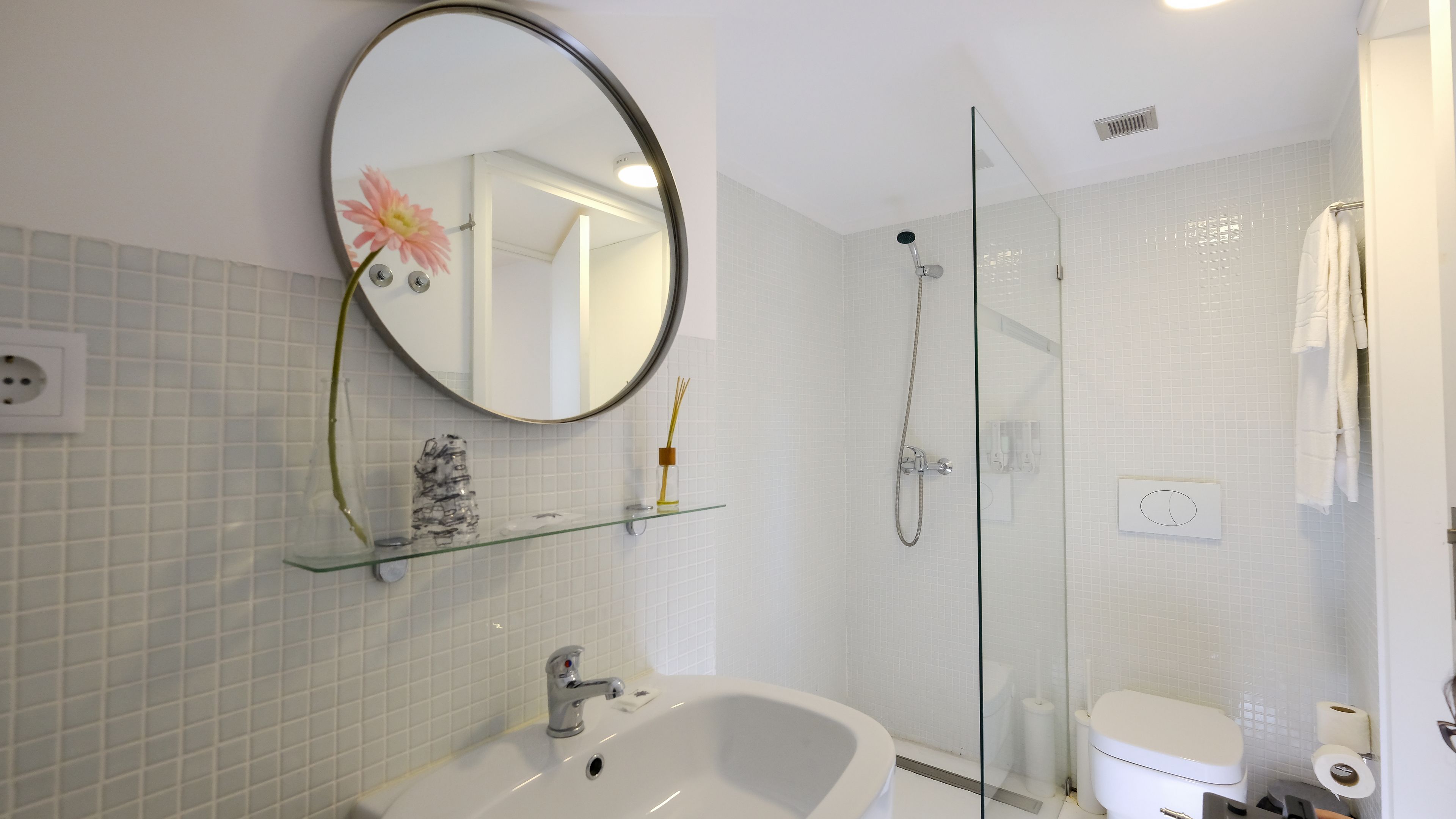 Une salle de bain équipée d’un lavabo, d’un miroir, d’une douche et de toilettes.