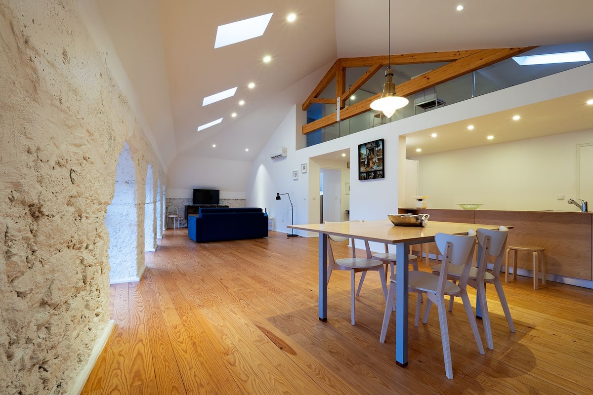 A spacious living area with a high ceiling, wooden beams, and a dining table with chairs.