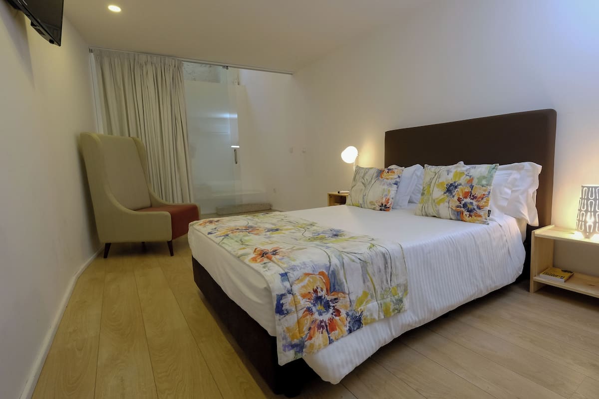 A hotel room with a bed, a chair, a nightstand, and a wall-mounted TV.