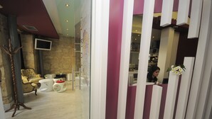 Un área de recepción de diseño moderno, con mostrador de recepción, zona de estar con sofá y una mesa de centro, y una pared de piedra al fondo.