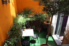A small patio area with a table and chairs, surrounded by potted plants and a green artificial turf.