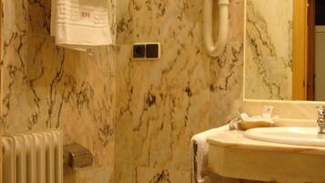 Un baño con pared de mármol, inodoro, bidé, lavamanos con espejo y un perchero para toallas.